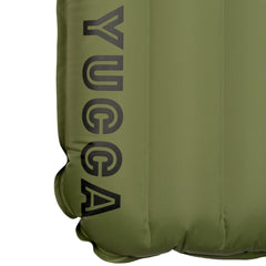 Close-up detail of the olive green Yucca Merlyn inflatable surf mat showing the black Yucca logo printed along the lower edge. Vertical air chambers and welded seams highlight the mat’s durable inflatable construction and minimalist branding.