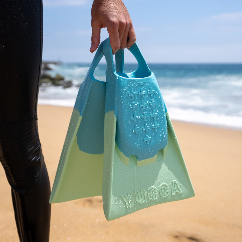 Person holding Yucca Karam Short Blade Fins - Soft Flex - Yucca Fins on a beach with ocean view