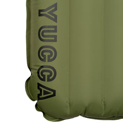 Close-up detail of the olive green Yucca Merlyn inflatable surf mat showing the black Yucca logo printed along the lower edge. Vertical air chambers and welded seams highlight the mat’s durable inflatable construction and minimalist branding.