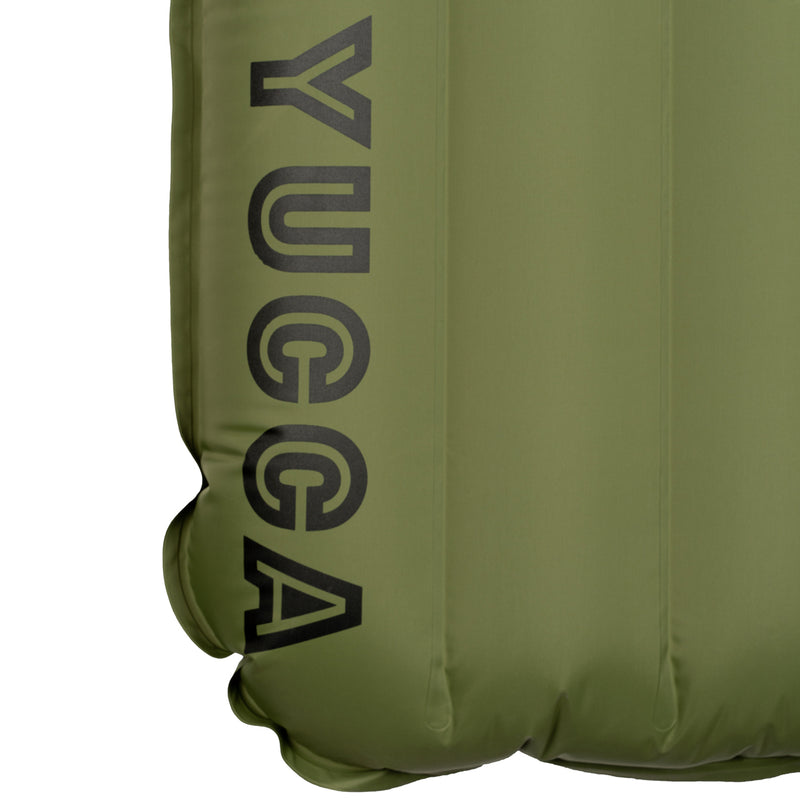 Close-up detail of the olive green Yucca Merlyn inflatable surf mat showing the black Yucca logo printed along the lower edge. Vertical air chambers and welded seams highlight the mat’s durable inflatable construction and minimalist branding.