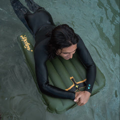 Person in a wetsuit lying on an inflatable surf mat in water
