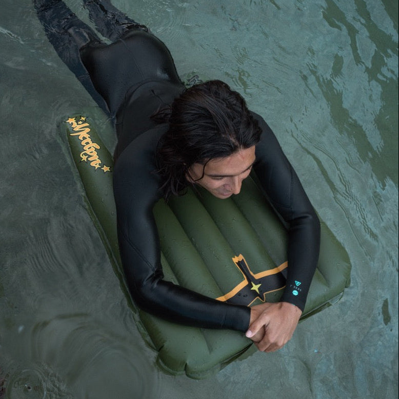 Person in a wetsuit lying on an inflatable surf mat in water