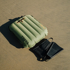 Inflatable green mat and black fins on sandy ground