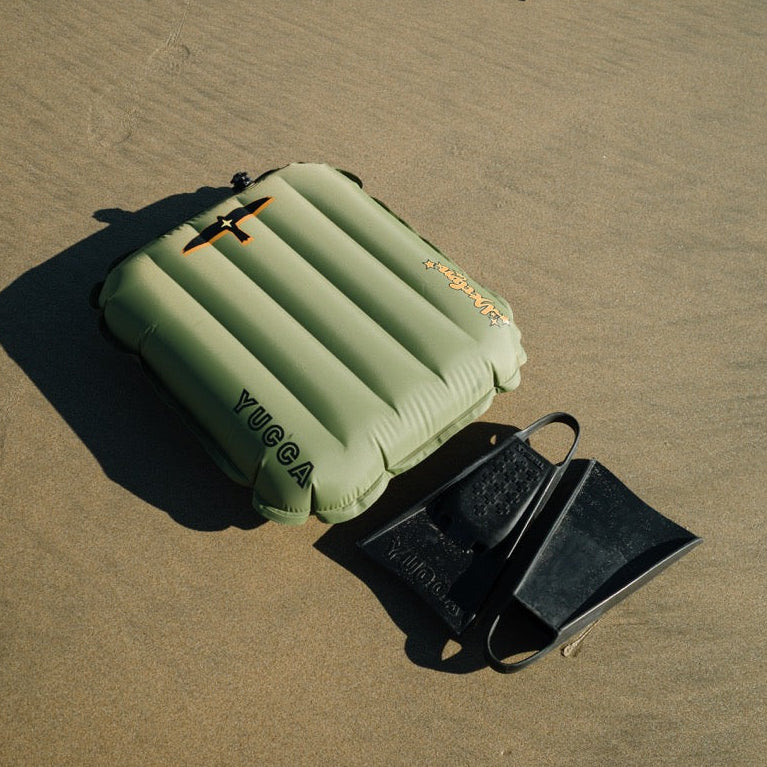 Inflatable green mat and black fins on sandy ground